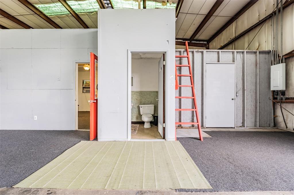 An interior view shows a bathroom, a doorway, and a ladder inside a warehouse space — 33144 MCCABE ROAD, SAN ANTONIO, FL