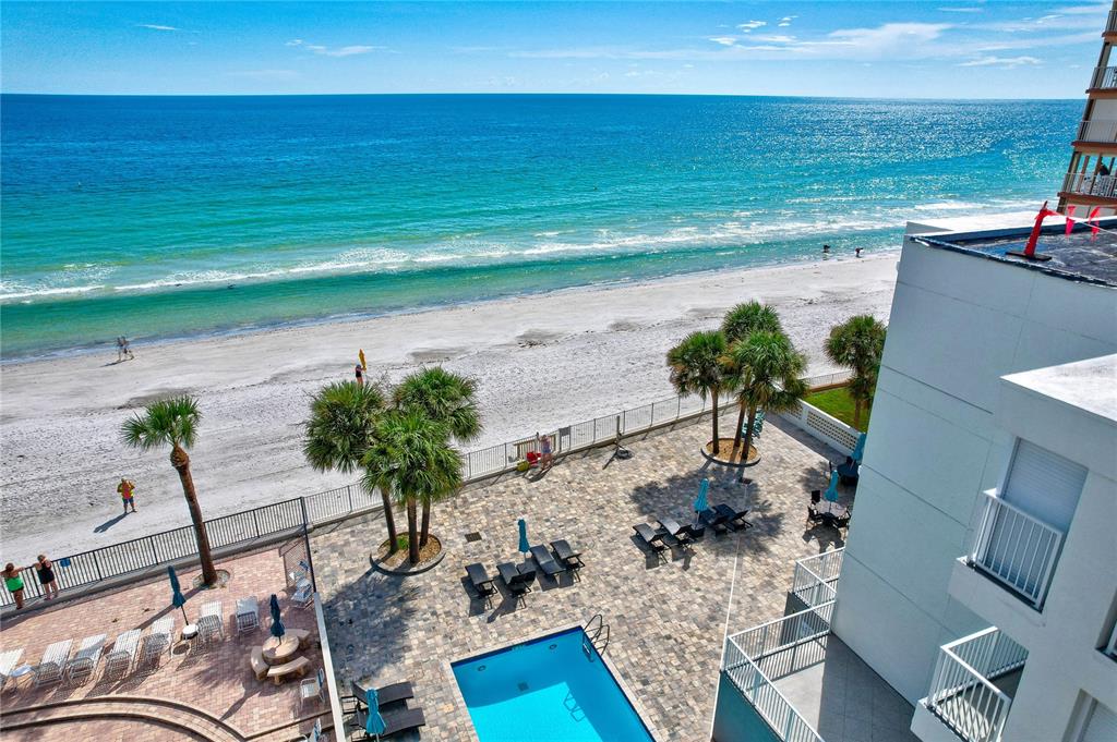 An elevated view shows a swimming pool, patio furniture, palm trees, and a sandy beach — 16332 GULF BOULEVARD UNIT 1C, REDINGTON BEACH, FL