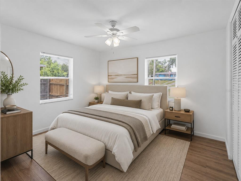 A bedroom features a bed with neutral bedding, two nightstands, a bench, and a ceiling fan — 572 E NORMANDY BOULEVARD, DELTONA, FL