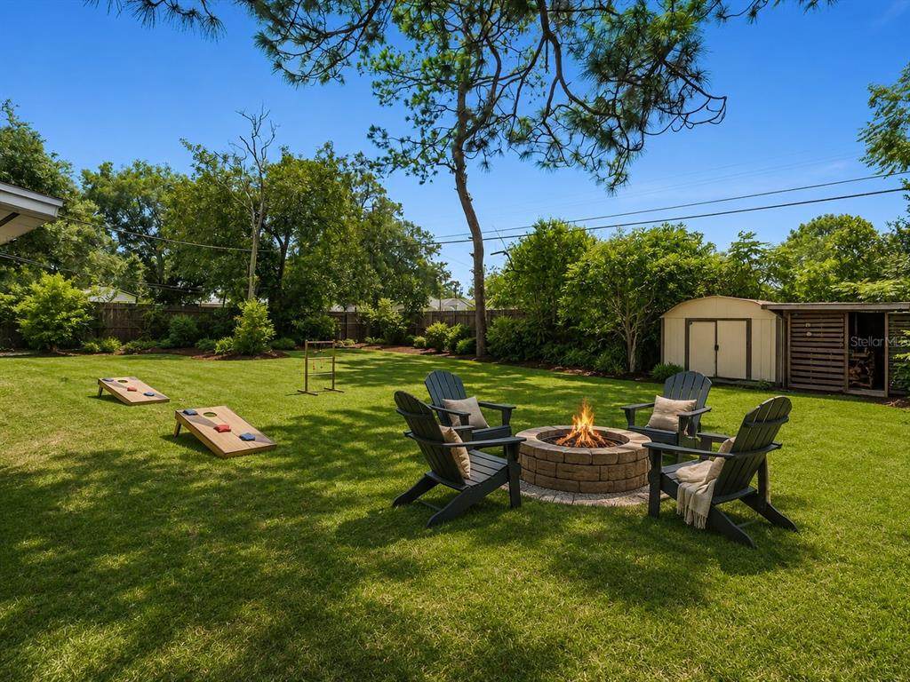 A backyard features a stone fire pit with four chairs, lawn games, and a storage shed — 572 E NORMANDY BOULEVARD, DELTONA, FL