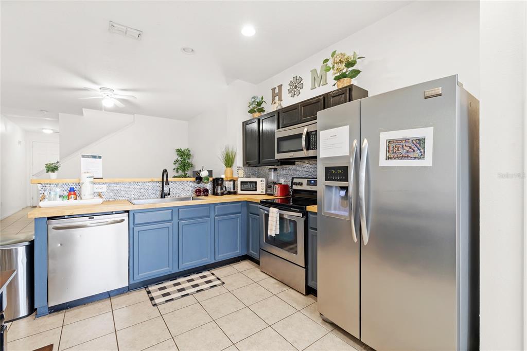 A kitchen features blue lower cabinets, stainless steel appliances, and a light wood countertop — 2685 ANDROS LANE, KISSIMMEE, FL