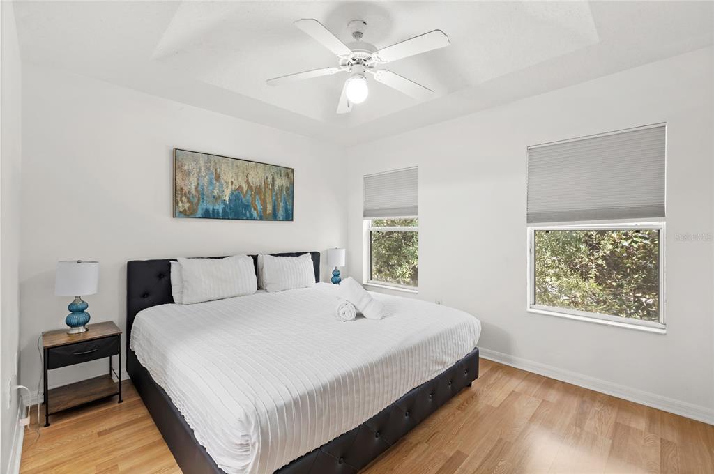 A bedroom features a king-sized bed with a dark tufted frame, wood flooring, and windows — 2685 ANDROS LANE, KISSIMMEE, FL