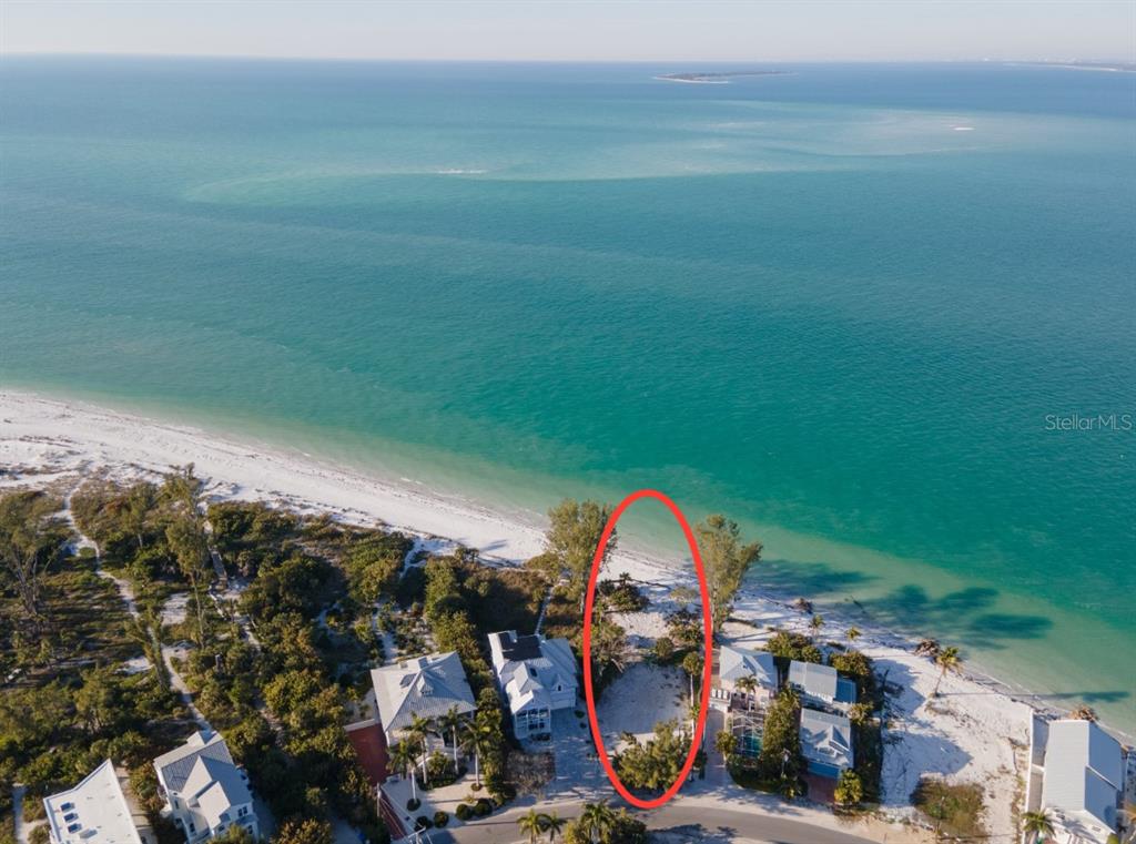 An aerial view shows a vacant beachfront lot situated between two houses along the coast — 831 NORTH SHORE DRIVE, ANNA MARIA, FL