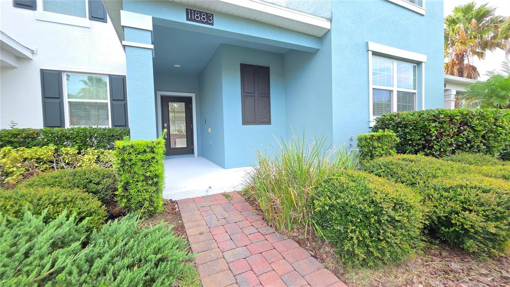 A blue exterior wall with a window and a landscaped garden bed with green shrubs — 11883 PULITZER PLACE, ORLANDO, FL