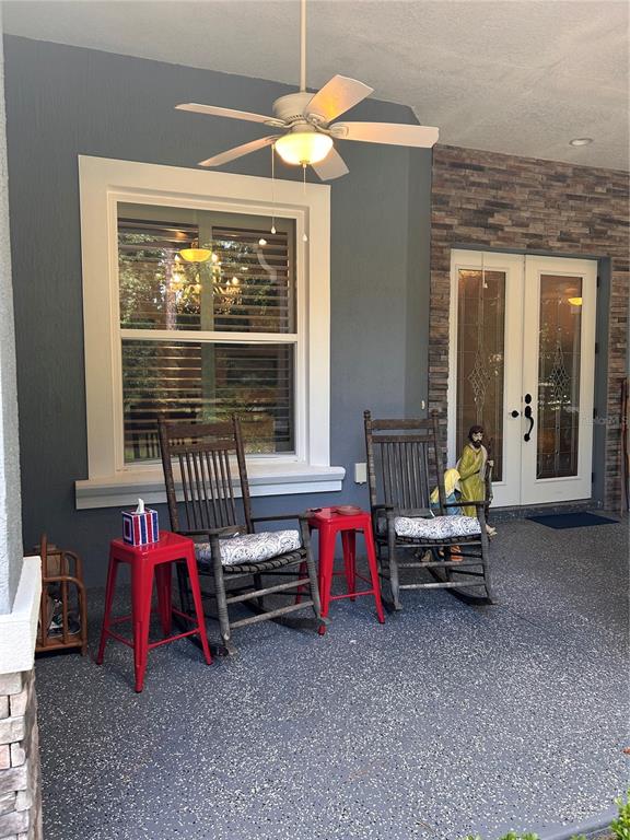 A covered porch features two wooden rocking chairs, red metal side tables, and stone accents — 12396 SW 61ST PLACE ROAD, OCALA, FL