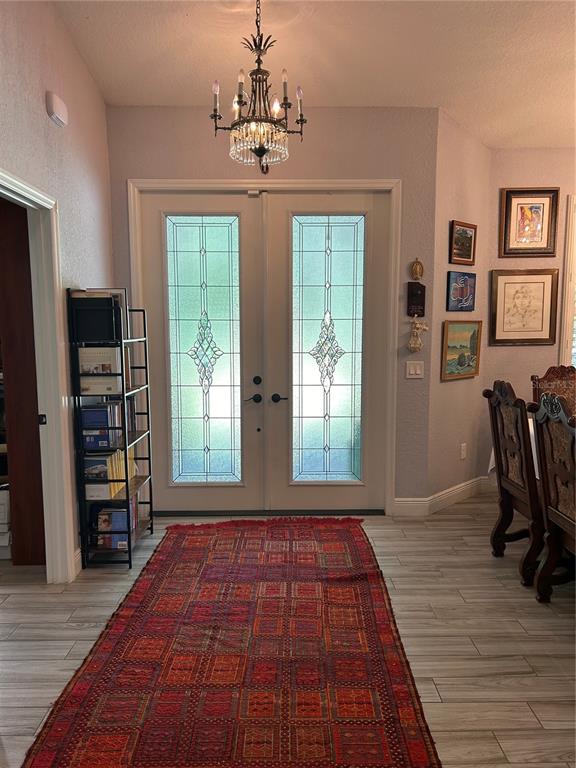 An entryway features a patterned rug, a chandelier, double glass doors, and a metal bookshelf — 12396 SW 61ST PLACE ROAD, OCALA, FL