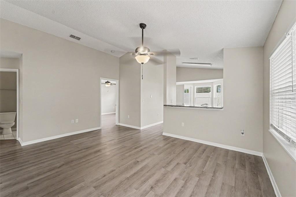 A kitchen with white cabinets, stainless steel appliances, and granite countertops opens to a living area — 10236 FLAGSHIP AVENUE, PORT RICHEY, FL