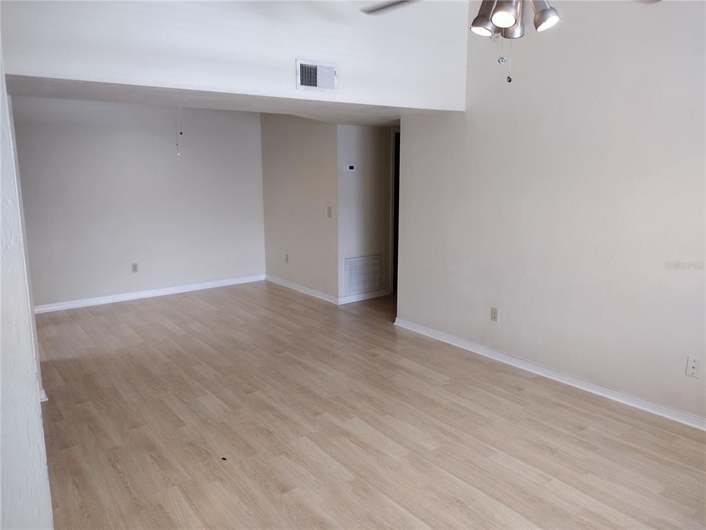 An empty room features light wood-look flooring, beige walls, and a vaulted ceiling with lighting — 2360 SW ARCHER ROAD UNIT 510, GAINESVILLE, FL