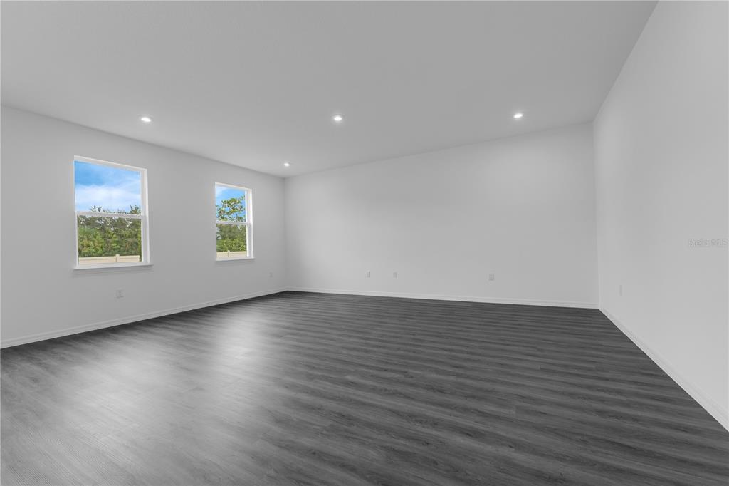 An empty room features white walls, recessed lighting, and dark wood-look flooring with two windows — 1812 HORSETAIL DRIVE, ST CLOUD, FL