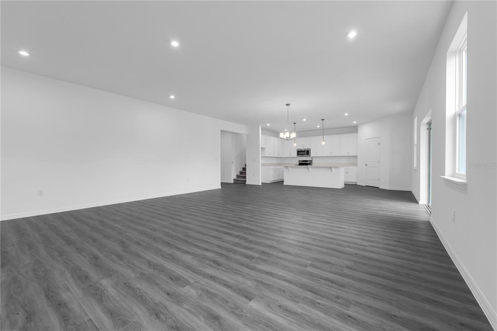 An open-concept living area features white walls, gray wood-look flooring, and a kitchen with white cabinets — 1812 HORSETAIL DRIVE, ST CLOUD, FL