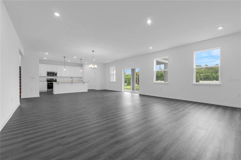 An open-concept living area features white walls, gray wood-look flooring, and a modern kitchen — 1812 HORSETAIL DRIVE, ST CLOUD, FL