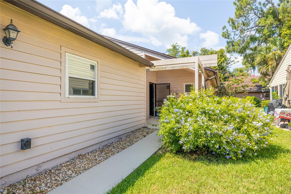 The exterior of a light-colored house features a concrete walkway and a flowering bush — 120 GULL CIRCLE N, DAYTONA BEACH, FL