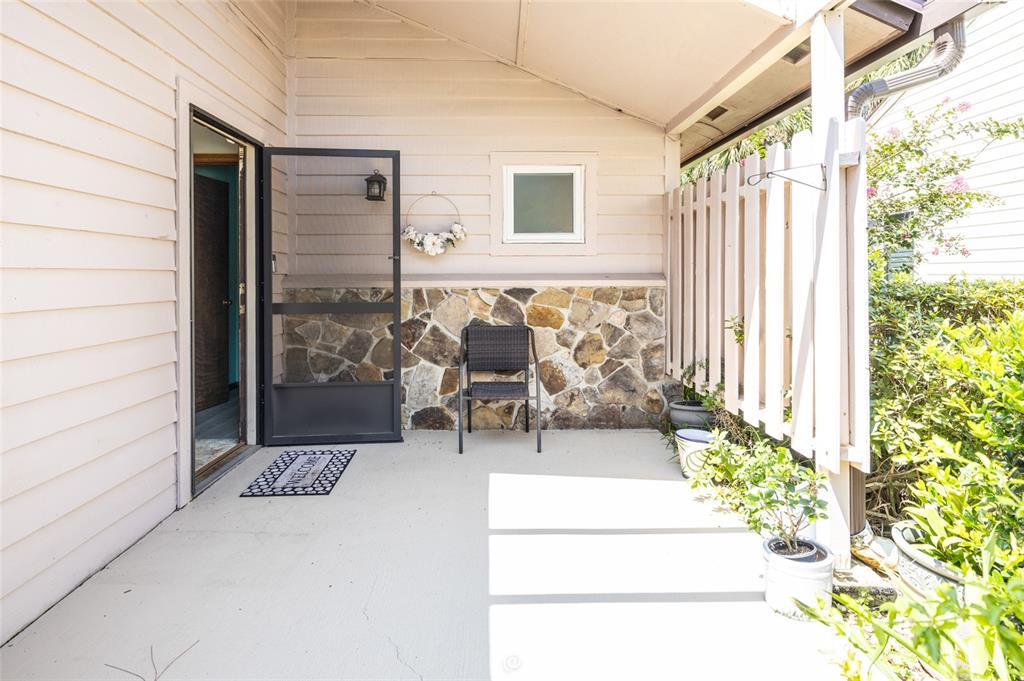 A covered patio features a stone accent wall, a single chair, and a screen door — 120 GULL CIRCLE N, DAYTONA BEACH, FL