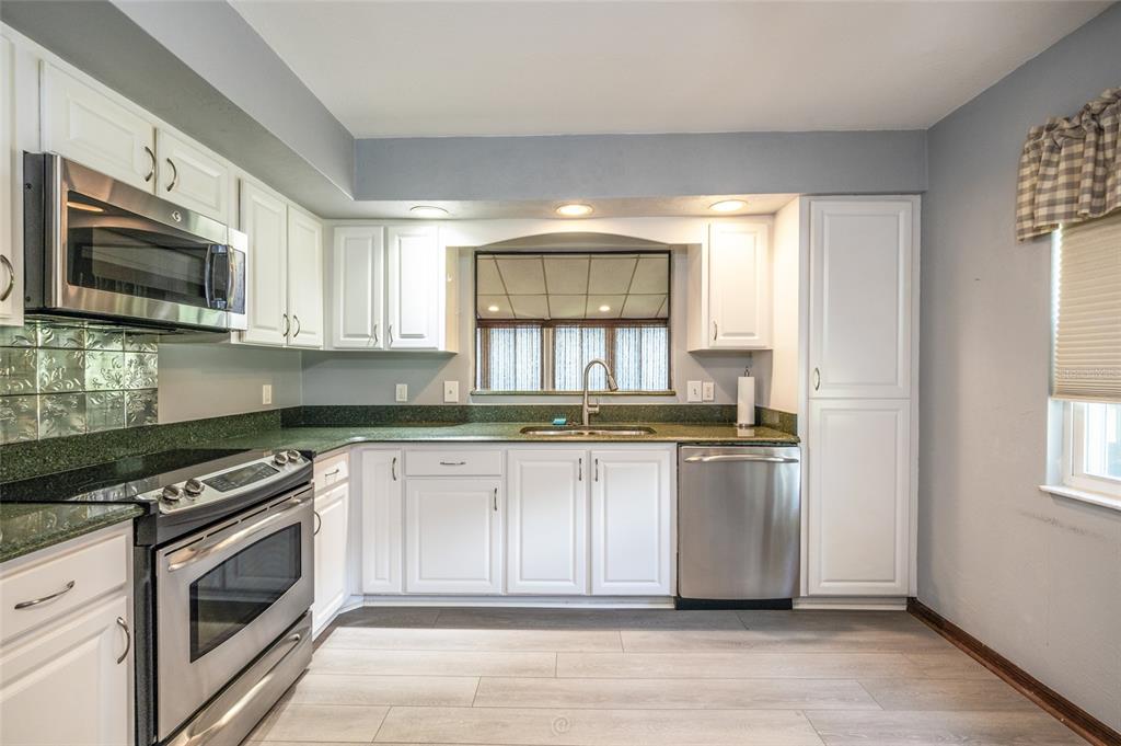 A kitchen features white cabinets, green countertops, stainless steel appliances, and light wood-look flooring — 120 GULL CIRCLE N, DAYTONA BEACH, FL