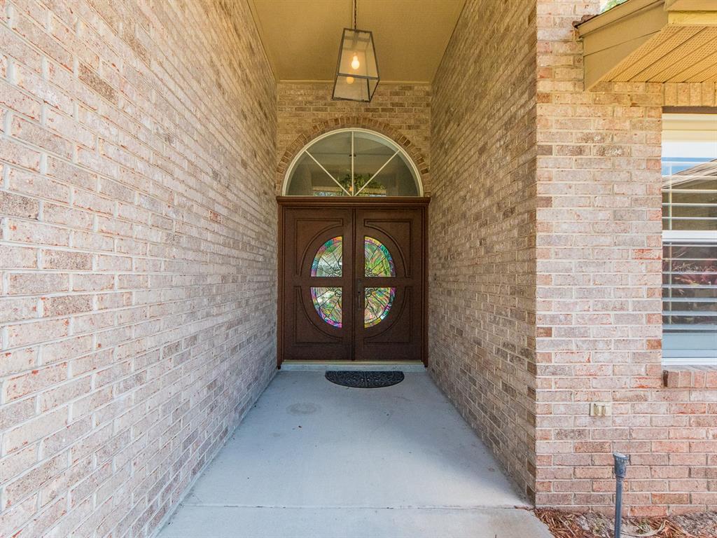 A brick-walled entryway features a double door with stained glass inserts and an arched transom — 2899 TURTLE TERRACE, PALM HARBOR, FL