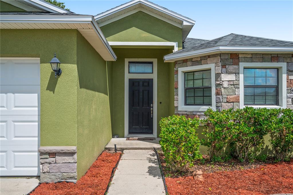 A green stucco house exterior features a black front door, stone accents, and a walkway — 7019 HEATHERBROOK DRIVE, LAKELAND, FL