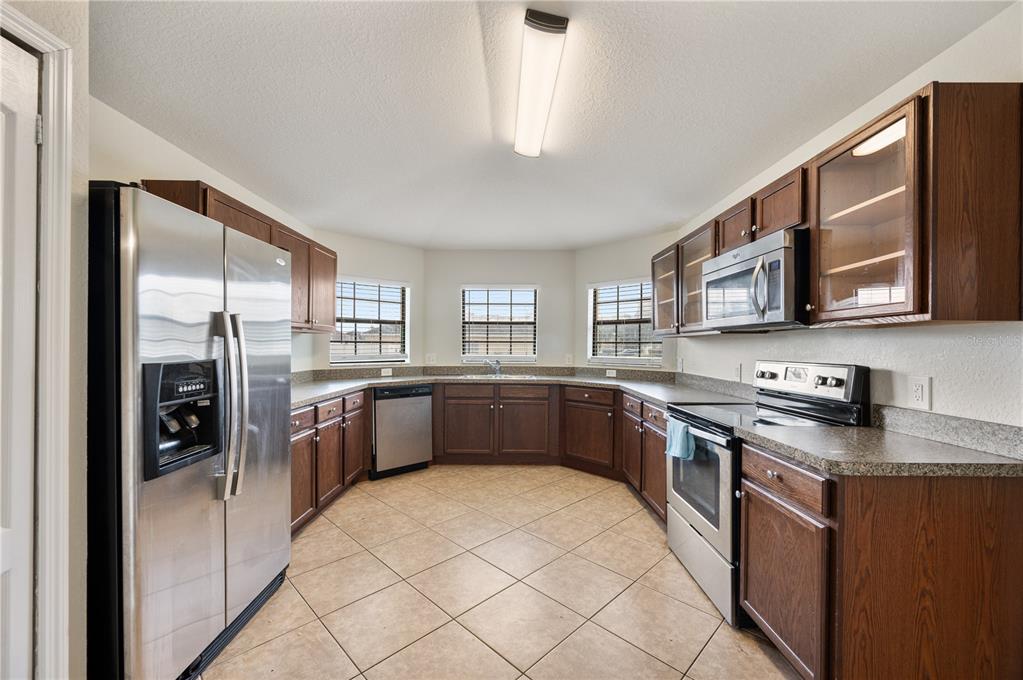 A kitchen features dark wood cabinets, stainless steel appliances, tile flooring, and three windows — 7019 HEATHERBROOK DRIVE, LAKELAND, FL