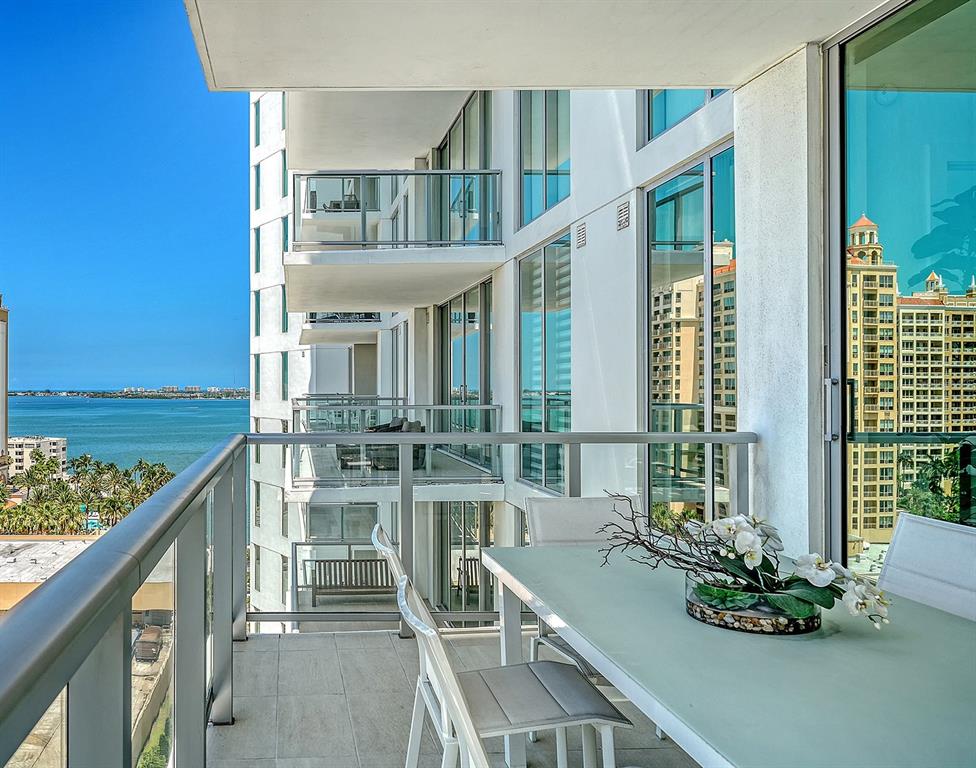 A balcony with a dining set overlooks a coastal city skyline and the ocean — 301 QUAY COMMONS UNIT 1007, SARASOTA, FL