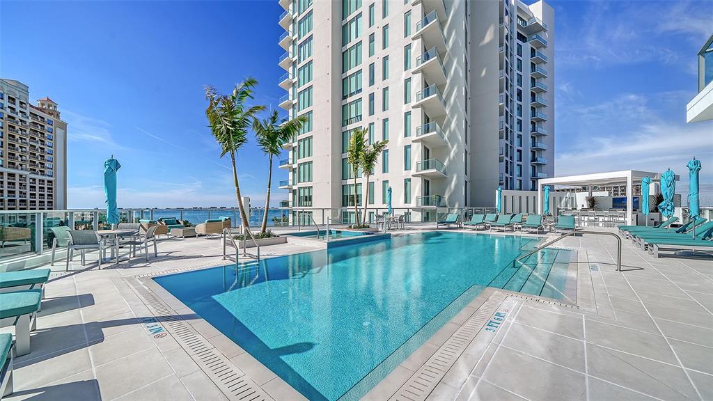 A swimming pool with lounge chairs and palm trees sits on a high-rise building terrace — 301 QUAY COMMONS UNIT 1007, SARASOTA, FL