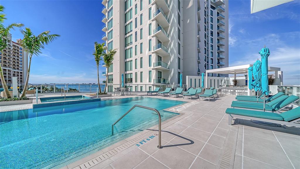 A swimming pool with lounge chairs on a patio next to a high-rise building — 301 QUAY COMMONS UNIT 1007, SARASOTA, FL