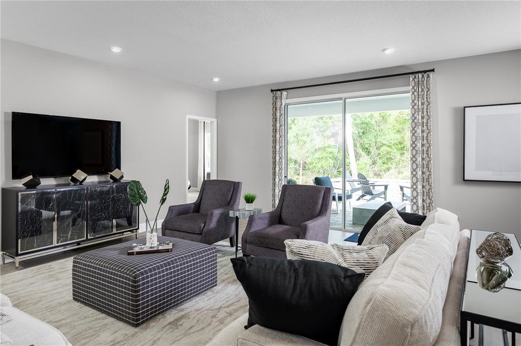 A living room features a large television, two grey armchairs, a patterned ottoman, and sliding glass doors — 8466 SWAN VIEW CIRCLE, LEESBURG, FL