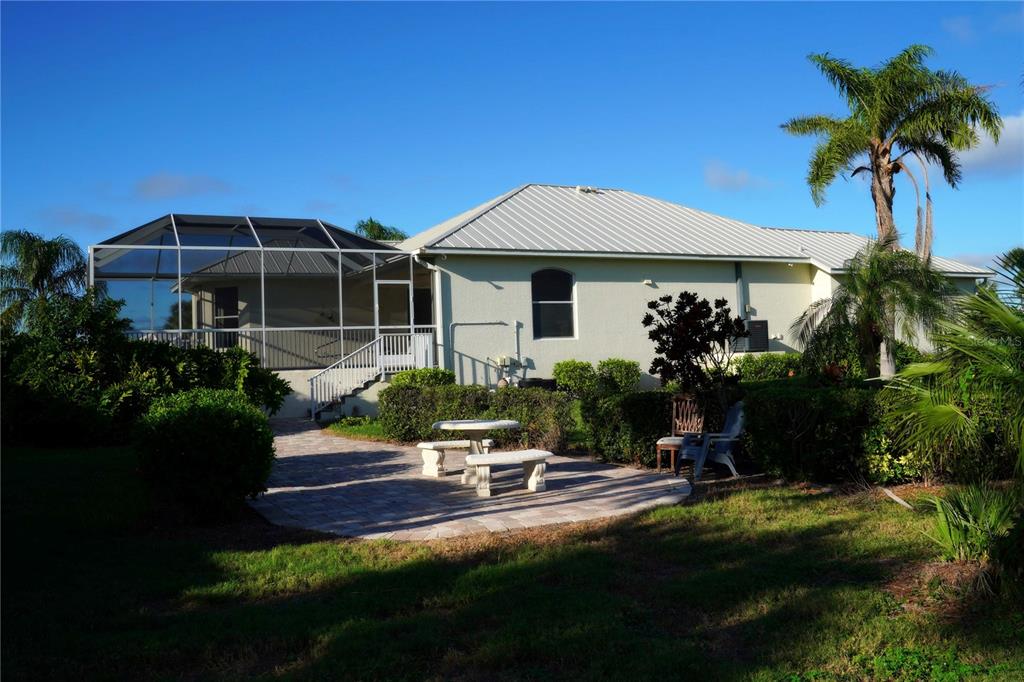 A backyard view of a house with a screened-in lanai, metal roof, and stone patio — 2 WINDWARD PLACE, PLACIDA, FL
