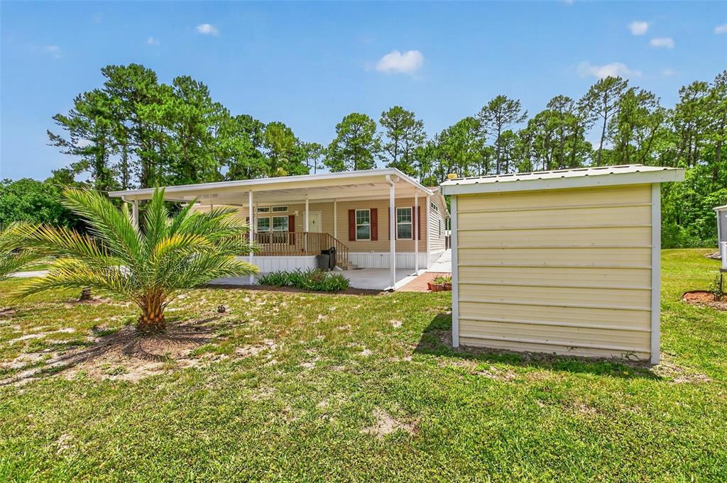 A mobile home with a covered porch and a detached metal shed in a yard — 101 TROUT TRAIL, CRESCENT CITY, FL