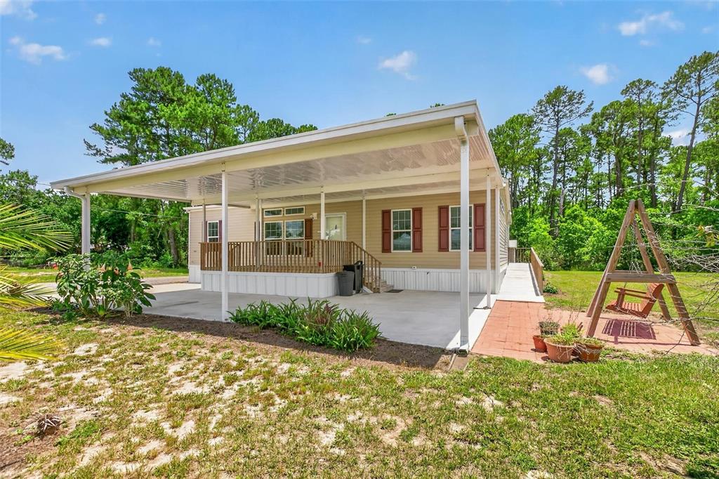 A manufactured home features a large covered patio, a wooden deck, and a swing set — 101 TROUT TRAIL, CRESCENT CITY, FL