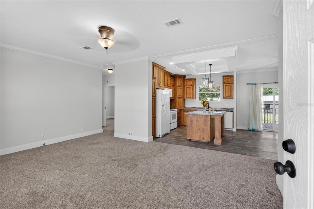 A carpeted living area opens into a kitchen with wood cabinets and a center island — 101 TROUT TRAIL, CRESCENT CITY, FL