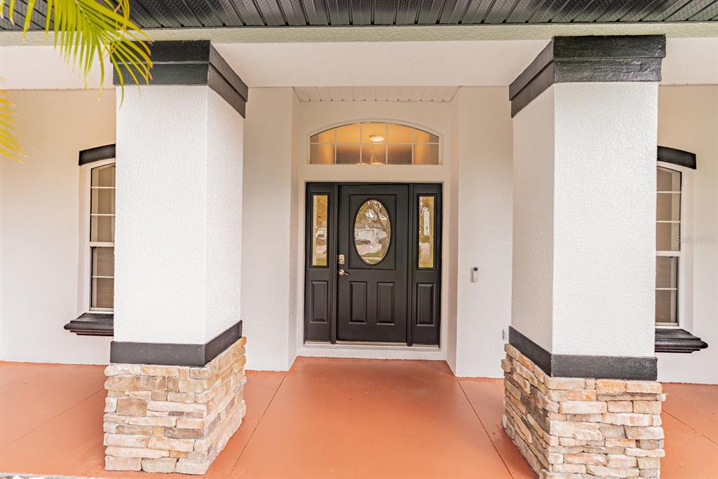 A covered front porch features two stone-based columns flanking a black front door with sidelights — 1670 TAYLOR RIDGE LOOP, KISSIMMEE, FL