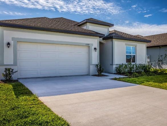 A single-story house exterior features a two-car garage, light stucco walls, and a concrete driveway — 6428 QUARTET STREET, MASCOTTE, FL