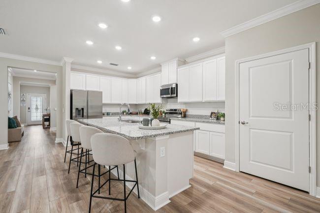 A kitchen features white cabinets, granite countertops, a center island with stools, and wood-look flooring — 6428 QUARTET STREET, MASCOTTE, FL