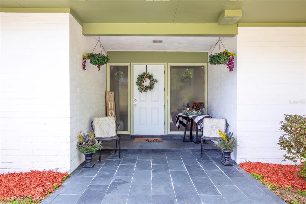 A covered front porch features a white door, two chairs, and a slate tile floor — 12182 SW STATE ROAD 45, ARCHER, FL