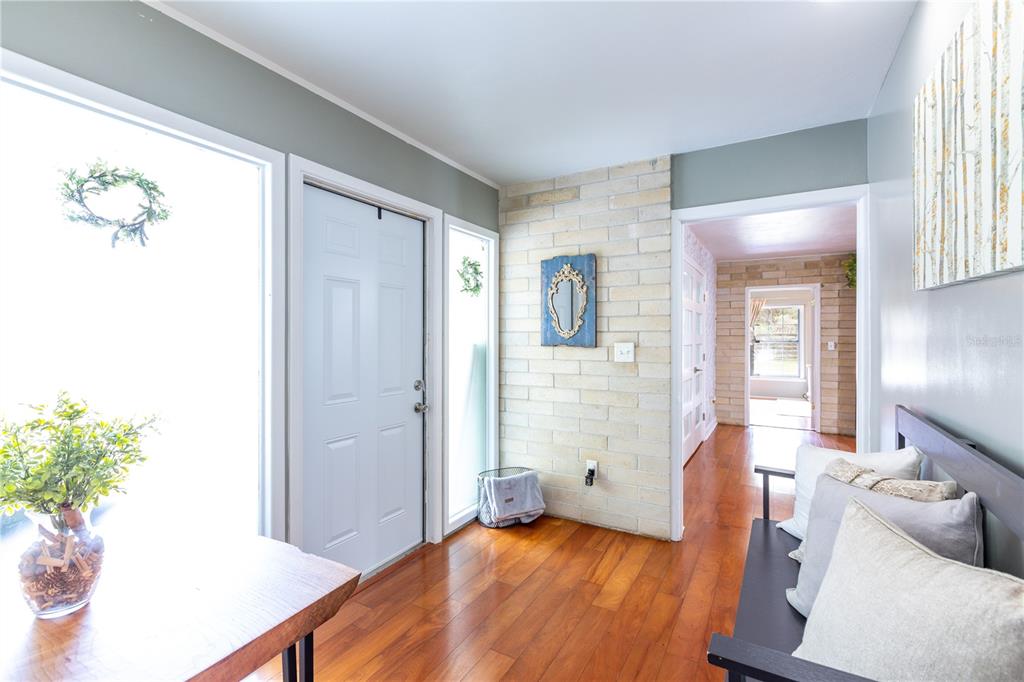 A bright entryway features hardwood floors, a white front door, and a light brick wall — 12182 SW STATE ROAD 45, ARCHER, FL