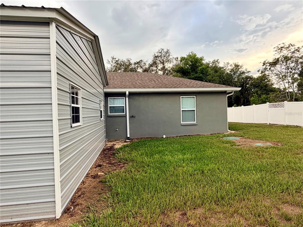 A view of a metal-sided structure adjacent to a gray stucco house with a lawn — 511 MOUNTAIN DRIVE, BABSON PARK, FL