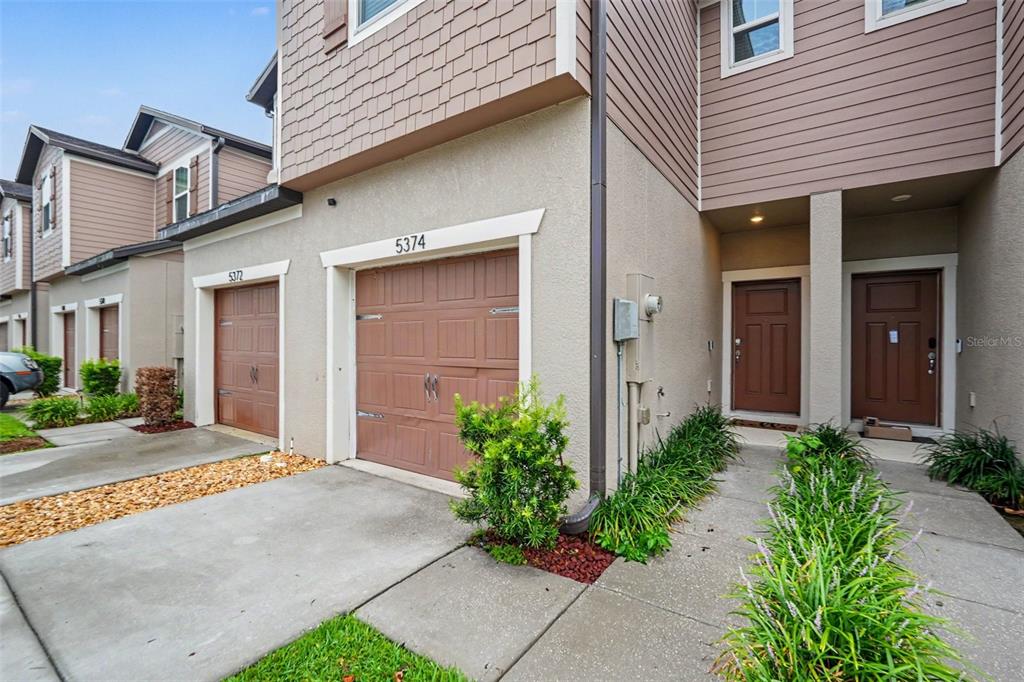 The exterior of two attached townhomes features brown garage doors, beige stucco, and siding — 5374 SYLVESTER LOOP, TAMPA, FL