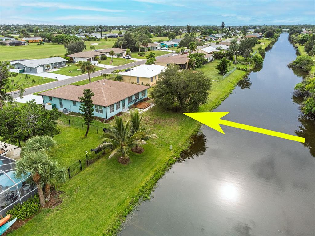 An aerial view shows a light blue house with a brown roof beside a canal — 199 CADDY ROAD, ROTONDA WEST, FL