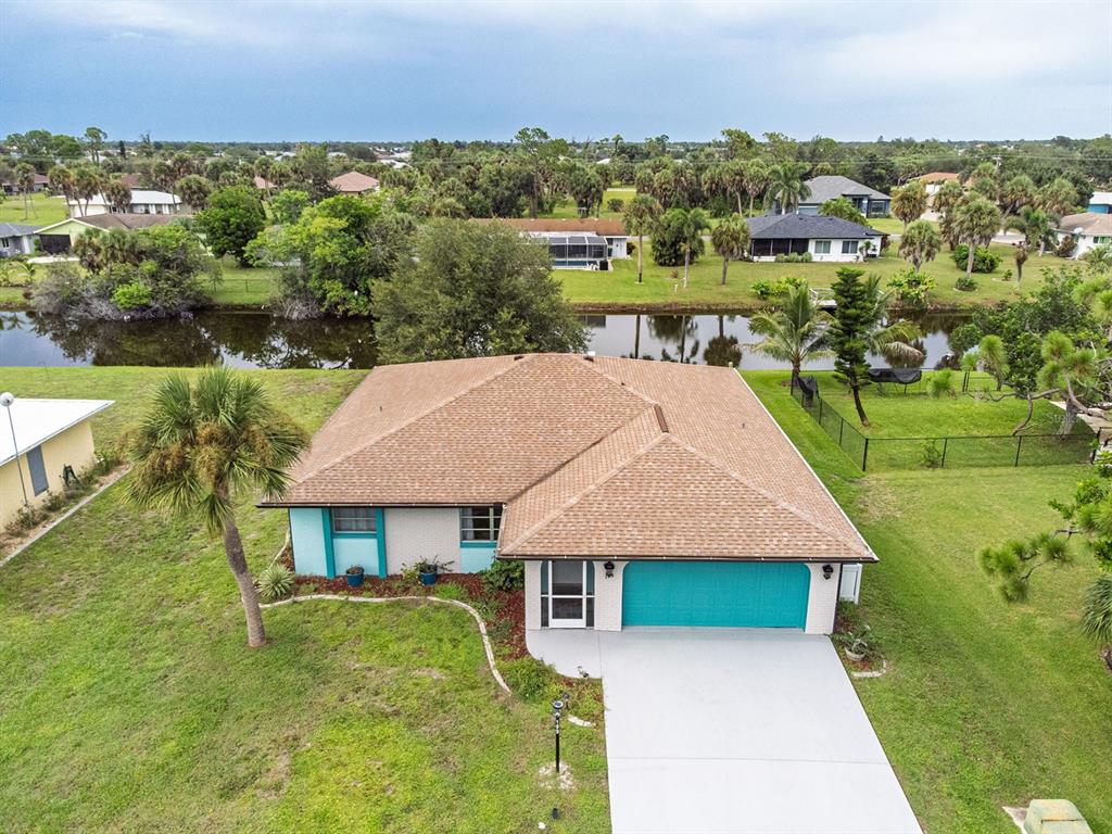 An aerial view of a single-story house with a brown roof, turquoise garage, and canal — 199 CADDY ROAD, ROTONDA WEST, FL