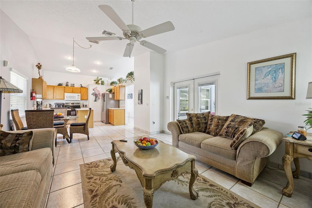 A living room with tile flooring, two beige sofas, a coffee table, and glass doors — 2948 PEMBRIDGE STREET, KISSIMMEE, FL