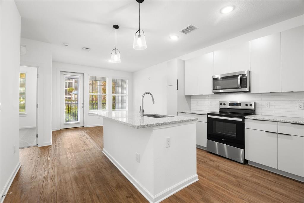 A modern kitchen features white cabinets, stainless steel appliances, a granite island, and wood flooring — 1700 RANCH ROAD UNIT A2-12210, NOKOMIS, FL