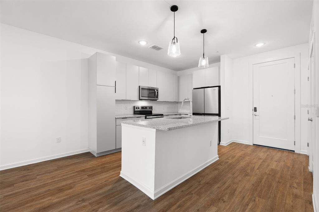 A modern kitchen features white cabinetry, stainless steel appliances, a granite island, and wood flooring — 1700 RANCH ROAD UNIT A2-12210, NOKOMIS, FL