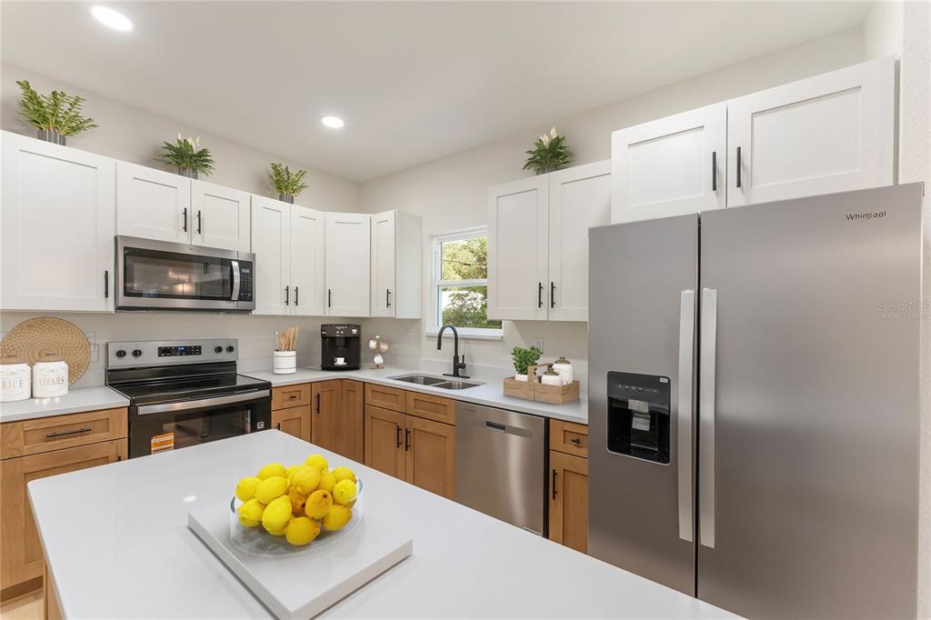 This open-concept living area features light wood flooring, a tray ceiling with a fan, and a kitchen — 925 NE 17TH DRIVE, GAINESVILLE, FL