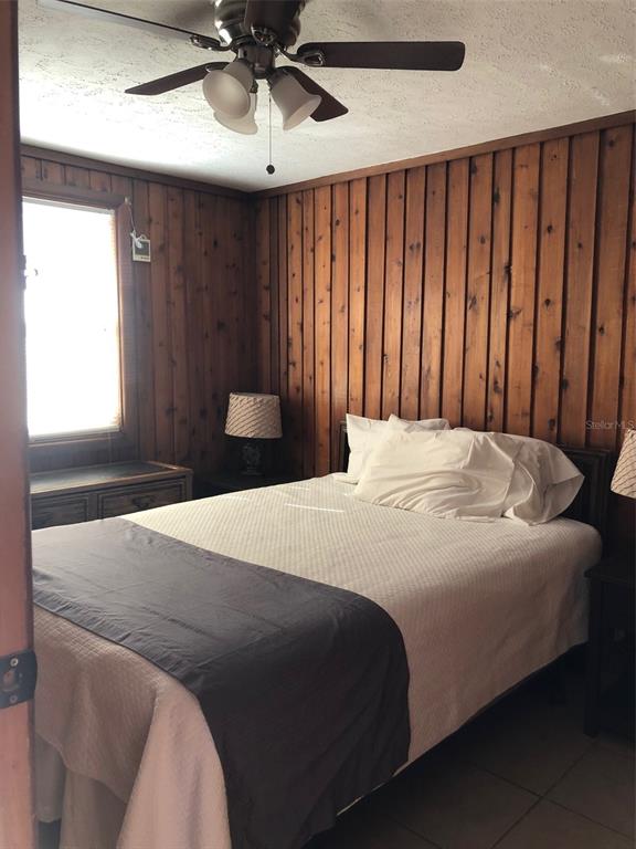 A bedroom features wood-paneled walls, a ceiling fan, and a bed with white bedding — 10301 US HIGHWAY 27 UNIT 100, CLERMONT, FL