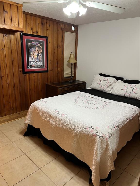 A bedroom features wood-paneled walls, a bed with a floral quilt, and tile flooring — 10301 US HIGHWAY 27 UNIT 100, CLERMONT, FL