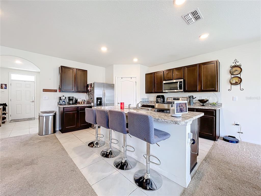 A kitchen features dark wood cabinets, granite countertops, a central island with barstools, and tile flooring — 1634 REDDISH EGRET COURT, DAVENPORT, FL