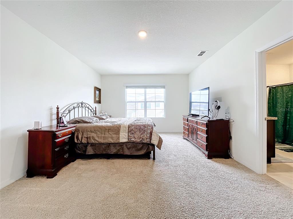 A bedroom features a metal-frame bed, dark wood furniture, beige carpeting, and an attached bathroom — 1634 REDDISH EGRET COURT, DAVENPORT, FL