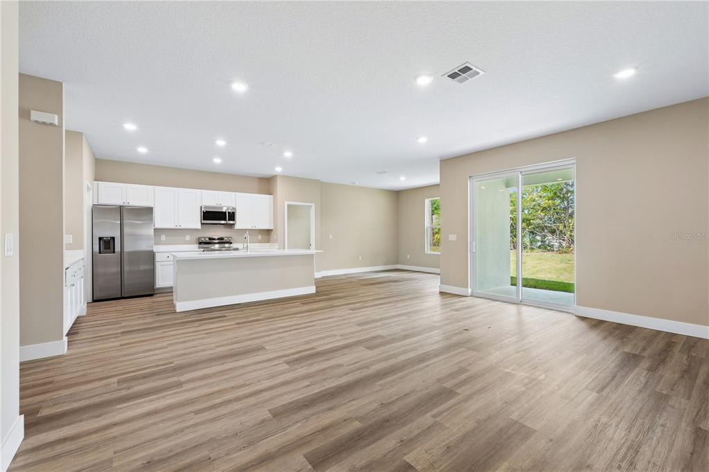 An open-concept kitchen and living area features white cabinets, stainless appliances, and wood-look flooring — 7 UPLAND PLACE, PALM COAST, FL