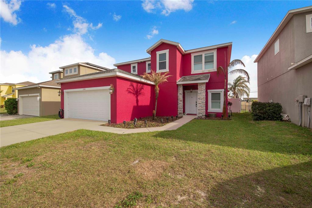 A two-story house with bright pink stucco siding, a white garage door, and stone accents — 1382 SALISBURY DRIVE, WINTER HAVEN, FL