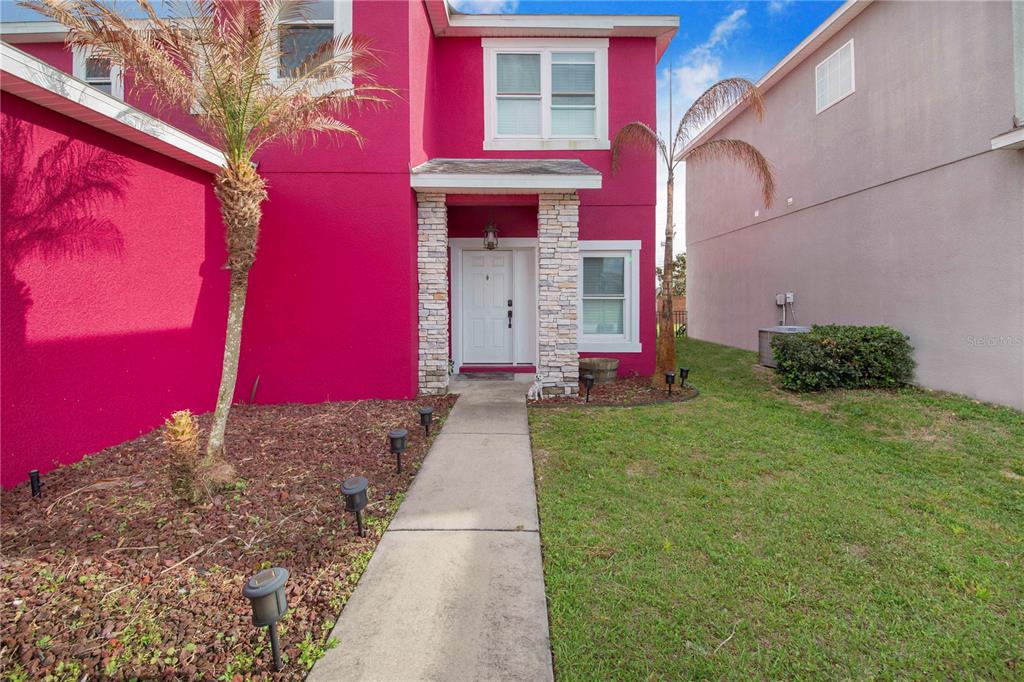 A bright pink two-story house features a stone-accented entryway and a concrete walkway — 1382 SALISBURY DRIVE, WINTER HAVEN, FL