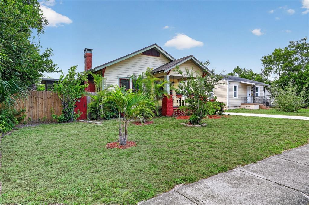 A yellow bungalow with a red brick chimney and porch pillars sits behind a grassy lawn — 2535 15TH AVENUE N, ST PETERSBURG, FL